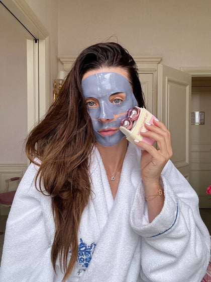 Woman wearing face mask using beauty device in robe.